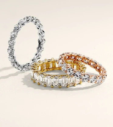 Three diamond rings in silver, gold, and rose gold on a beige background
